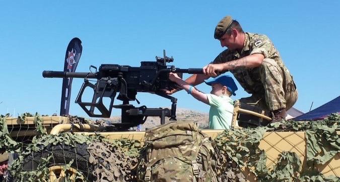 A soldier inviting a small child to handle a gun at the Armed Forces Day National Event in Llandudno, 2018