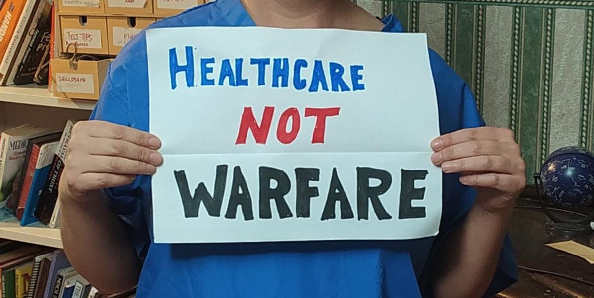 Hands holding a sign reading 'Healthcare Not Warfare'